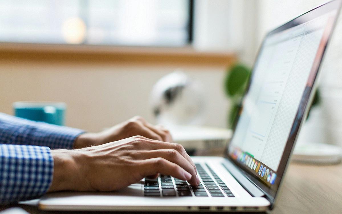 Close of photo of a laptop with a pair of hands using it